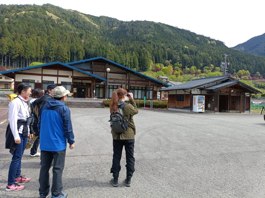 下呂市馬瀬の野鳥ウォッチングツアーで、森へ入る前に双眼鏡の使い方を教わりながら野鳥を探す初心者や参加者の様子。